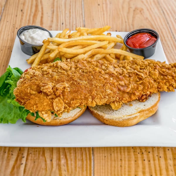Crispy fried fish sandwich with lettuce, fries, tartar sauce, and ketchup on a white plate.