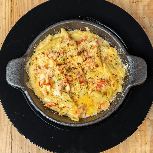 Jumby Bay Island Grill's lobster mac and cheese in a cast iron skillet on a black plate.