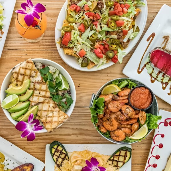 A wooden table laden with various seafood dishes, including grilled fish, shrimp, nachos, and a cocktail.