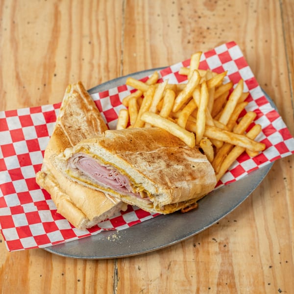 A Cuban sandwich with ham, cheese, and mustard, served with a side of golden french fries.
