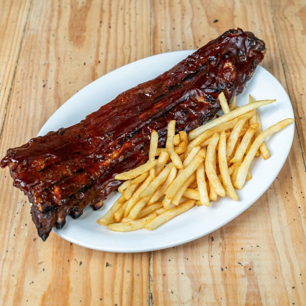 A full rack of BBQ ribs with a side of golden french fries on a white plate.