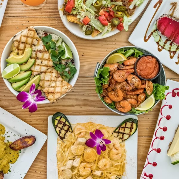 A wooden table laden with various seafood dishes, including grilled fish, shrimp, nachos, and pasta.